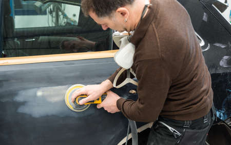 Car mechanic with dust mask grinds a car part in a service station - Serie car repair workshopのeditorial素材