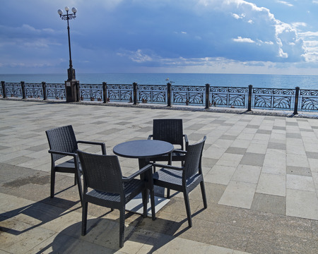 A table and four chairs on an empty seafront of the resort town of Sudak, Crimea.の写真素材