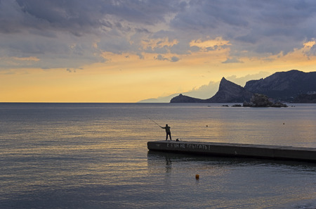 A lone fisherman on a breakwater. Evening in the Sudak bay, Crimea.の写真素材