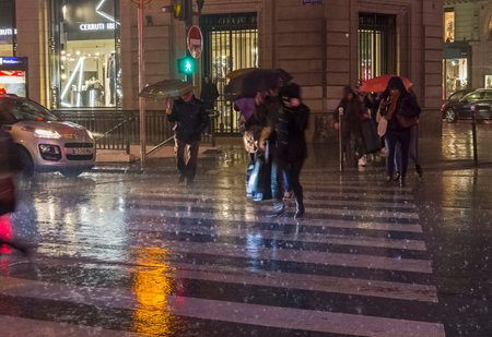 PARIS, FRANCE - DECEMBER 10, 2017: People cross the street in the pouring rain. Paris, Boulevard Haussmann, December evening.のeditorial素材