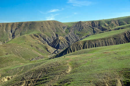 A semi-desert covered with fresh green grass in spring. Clay ravines with traces of soil erosion and weathering at the foot of Cape Meganom. Crimea, a sunny day in April.の写真素材