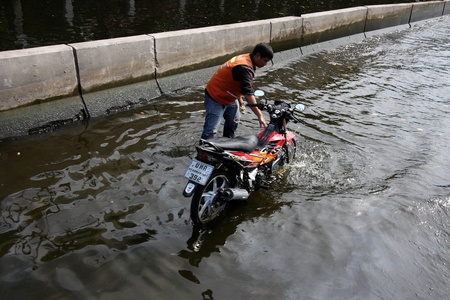 Bangkok, Thailand - November 20, 2011: A moto taxi driver is fixing his motorbike on an empty flooded street in Bangkok, Thailandのeditorial素材