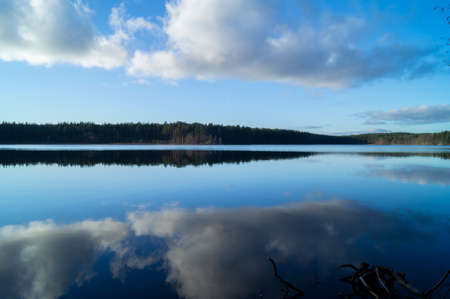 Nordic lake in autumn forest with reflection in blue waterの写真素材