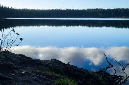 Nordic lake in autumn forest with reflection in blue waterの写真素材
