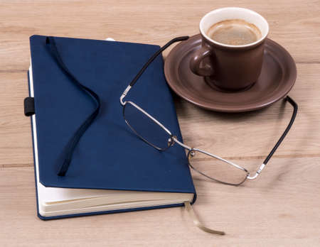 Image of notebook closed coffee cup pen and glasses.の写真素材