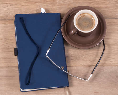 Image of notebook closed coffee cup pen and glasses.の写真素材