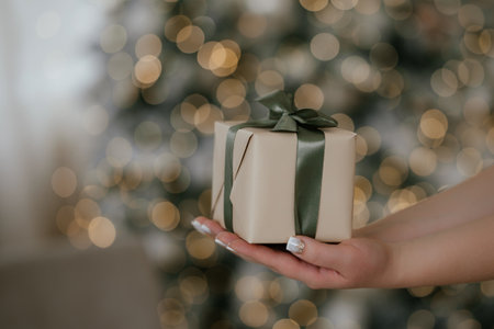 Hands Holding Gift Box with Green Ribbon in Festive Settingの写真素材