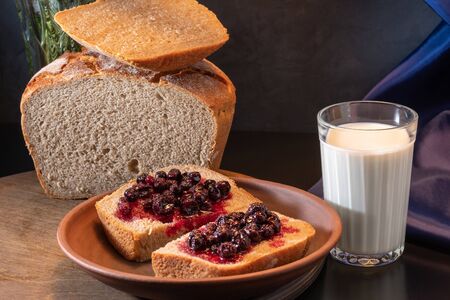 Homemade bread, a glass of milk, a clay jug and berries of black currant with sugar on a background...