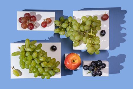 Grapes and apples on white parallelepipeds on a blue background, top viewの写真素材