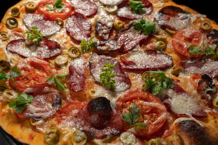 Homemade pizza with smoked meat, tomatoes, olives and herbs.の写真素材