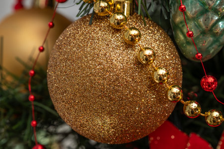 Golden Christmas Ornament Hanging From Green Christmas Tree With Beads and Festive Glow.の写真素材