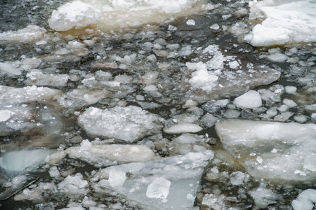 Chunks of melting ice and scattered ice floes drift across dark river water, illustrating...