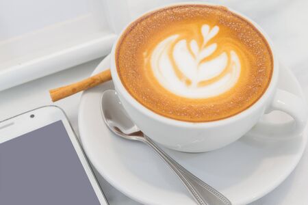 Texture of Tulip Flower on Top Hot Coffee in The Cup, Latte Art, Rosetta on Plate with Spoon, Cinnamon and Smart Mobile Phone for Morning or Relax Time (Selective Focus)の写真素材