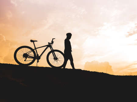 The mountain biker's silhouette lifts the bike happily that he has succeeded. from the competition On the high mountains in the evening, it is colorful.の写真素材