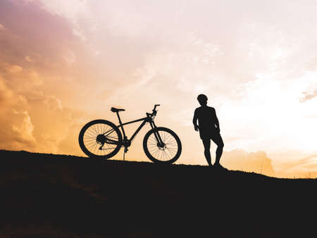 The mountain biker's silhouette lifts the bike happily that he has succeeded. from the competition On the high mountains in the evening, it is colorful.の写真素材