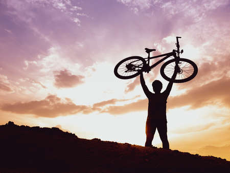 The mountain biker's silhouette lifts the bike happily that he has succeeded. from the competition...