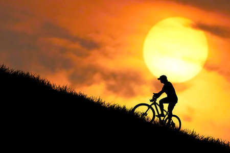 A man riding a mountain bike up a steep hill takes effort. Patience for success. concept of effort to success from the competition On the high mountains in the evening, it is colorful.の写真素材