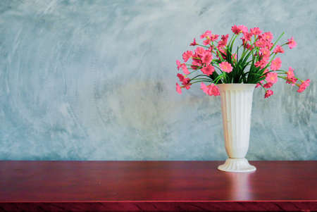 A vase of red flowers is placed on the table against a backdrop of a plaster wall.の写真素材