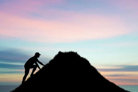 The man was climbing to the top of the mountain with a beautiful light effort. Silhouette of man climbing up steep edge of mountain. Fit young determined man climbing to top of mountain. People Never giving up, strength and power.の写真素材