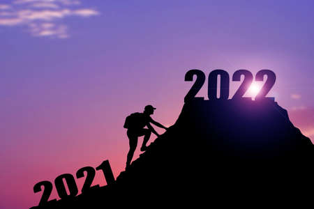 Welcome merry Christmas and happy new year in 2022,Silhouette Man from 2021cliff to 2022 cliff with cloud sky and sunlight. Man holding 2022 banner on top of mountain. Happy New Year 2022 concept. Rock climbing man finds 2022 sign on top of mountain.の写真素材