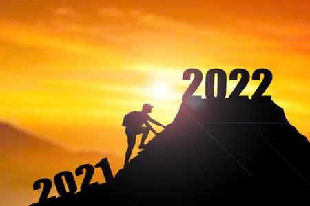 Welcome merry Christmas and happy new year in 2022,Silhouette Man from 2021cliff to 2022 cliff with cloud sky and sunlight. Man holding 2022 banner on top of mountain. Happy New Year 2022 concept. Rock climbing man finds 2022 sign on top of mountain.の写真素材