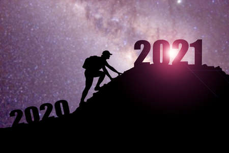 Welcome merry Christmas and happy new year in 2021,Silhouette Man from 2020cliff to 2021 cliff with cloud sky and sunlight. Man holding 2021 banner on top of mountain. Happy New Year 2021 concept.の写真素材
