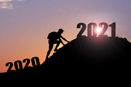 Welcome merry Christmas and happy new year in 2021,Silhouette Man from 2020cliff to 2021 cliff with cloud sky and sunlight. Man holding 2021 banner on top of mountain. Happy New Year 2021 concept.の写真素材