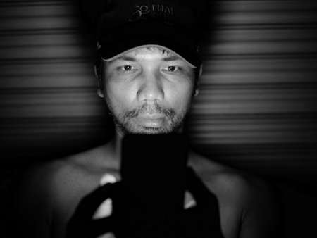 An Asian man looks at his mobile phone in a dark corner with homesickness.の写真素材