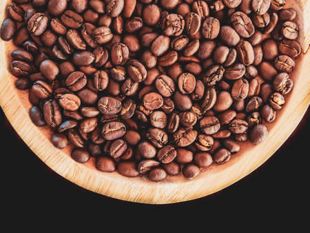 medium roast coffee beans in a wooden plate on a black backgroundの写真素材