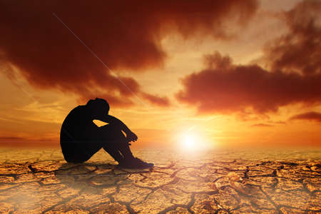 People sit with their heads down and hopeful in a dry land because of the drought there is no rain for a long time. Global warming and drought conceptの写真素材