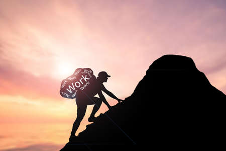 A man carrying a heavy bag climbs to the top of a mountain. hard working man concept for success. The concept works hard.の写真素材