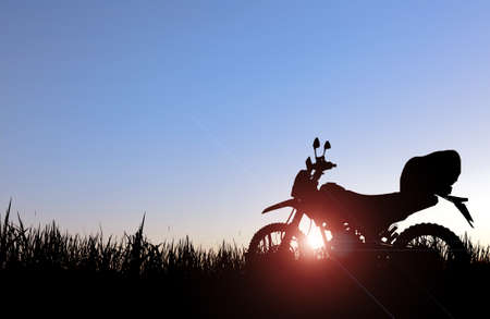 An adventurous touring silhouette of a off-road motorcycle parked in a field in the evening.の写真素材