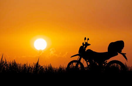 An adventurous touring silhouette of a off-road motorcycle parked in a field in the evening.