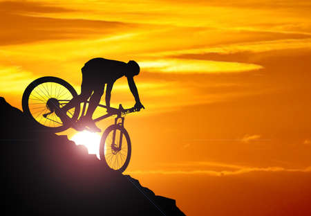 A silhouette of a cyclist descending from the mountain in the evening ...