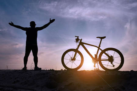 A man raising his hands happily exercising on a bicycle in the evening.の写真素材