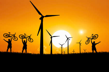 Silhouettes of touring cyclists. Cyclist silhouettes happily lift their bikes in a windmill that generates electricity. The concept is happy because of clean energy.の写真素材