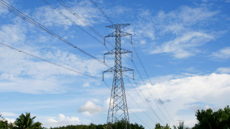 High voltage power poles in rural Thailand. High-voltage power lines passing through a plowed field, on the background of a beautiful cloudy sky.の写真素材