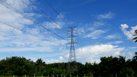 High voltage power poles in rural Thailand. High-voltage power lines passing through a plowed field, on the background of a beautiful cloudy sky.の写真素材