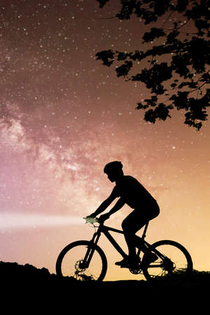 Silhouette of a cyclist in the night sky with stars.の写真素材