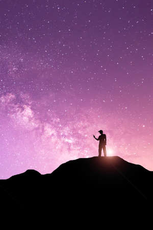 Night landscape with Milky Way. Silhouette of a standing young man with raised up arms on the mountain. Beautiful Universe. Travel backgroundの写真素材