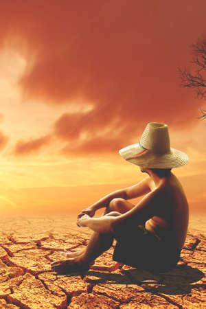 Woman in straw hat sitting on a cracked ground and looking at the sunsetの写真素材