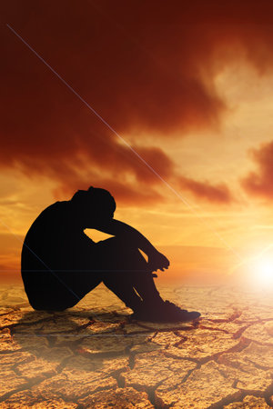 People sit with their heads down and hopeful in a dry land because of the drought there is no rain for a long time. Global warming and drought conceptの写真素材