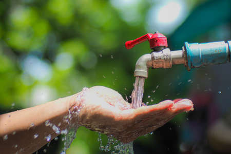 Water concept in everyday life. Hands supporting the water flowing from the faucet. water splashing from the tapの写真素材