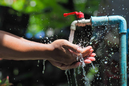 Water concept in everyday life. Hands supporting the water flowing from the faucet. water splashing from the tapの写真素材