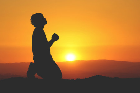 Silhouette of a man meditating on a hill at sunsetの写真素材