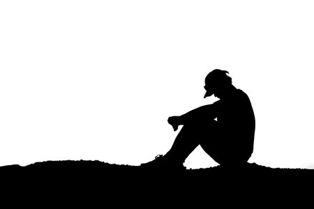Silhouette of a man sitting on the ground and looking downの写真素材