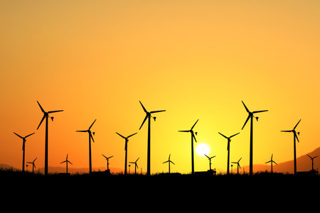 Silhouetted wind turbines against a vibrant orange sunset, highlighting renewable energy and sustainable power in a scenic landscape.の写真素材