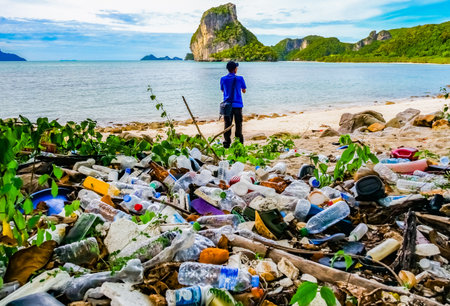 A man stands on a beach littered with plastic waste, highlighting environmental pollution against a backdrop of scenic mountains and ocean.の写真素材