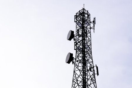 A tall communication tower with antennas and dishes against a clear sky, used for telecommunication...