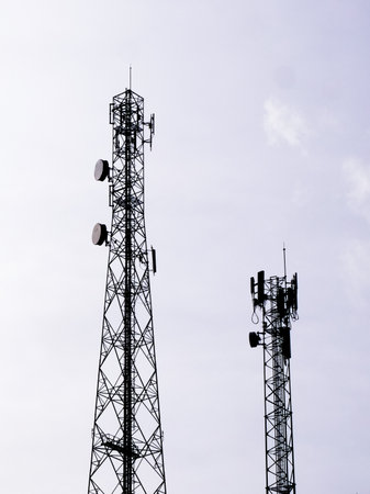 Two tall communication towers with antennas and dishes, set against a clear sky, representing modern telecommunication and broadcasting infrastructure.の写真素材